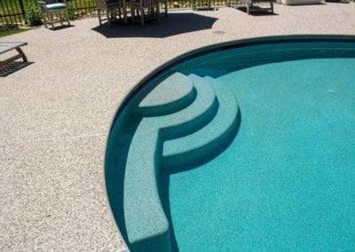 Curved pool steps constructed by a reputable pool builder lead into a turquoise swimming pool with a playground in the background.