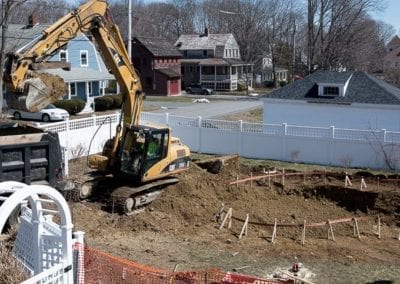 Excavator digging a large hole for a swimming pool installation in a residential backyard.