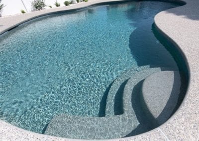 Curved swimming pool with built-in steps and clear blue water, crafted by a renowned pool builder.