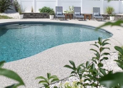 A backyard swimming pool installed by a reputable pool company, with a patio area and lounging chairs surrounded by a white fence.