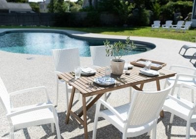 Outdoor dining setup by a swimming pool, crafted by a top pool company, on a sunny day.