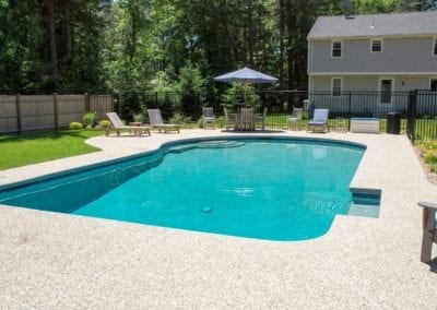 Backyard swimming pool constructed by a top-rated pool company with lounging chairs on a sunny day.