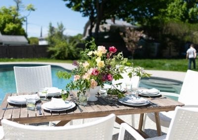 Outdoor dining setup by a swimming pool with a bouquet of flowers on the table and a person in the background.