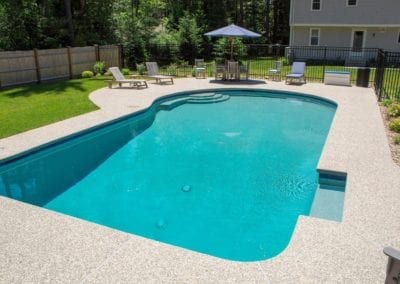 A backyard swimming pool created by a notable pool builder on a sunny day with patio furniture and an umbrella in the background.