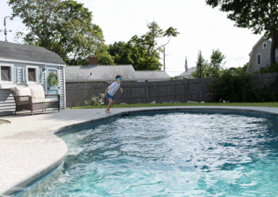 A child jumping into a backyard swimming pool, constructed by a top-rated pool company, on a sunny day.