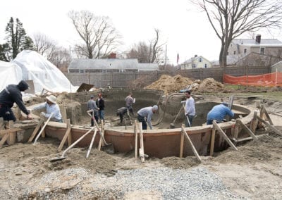 Construction workers from a pool company pouring concrete for a foundation at a building site.