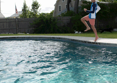 A person jumping into an outdoor swimming pool designed by a renowned pool company.