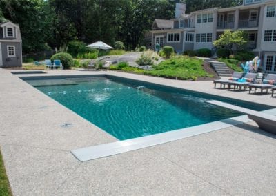 A backyard swimming pool, crafted by a top-rated pool company, with lounge chairs beside a large house.