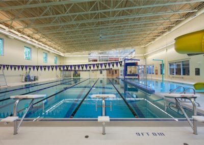 Indoor swimming pool with lanes, starting blocks, and a water slide in the background, constructed by a professional pool company.