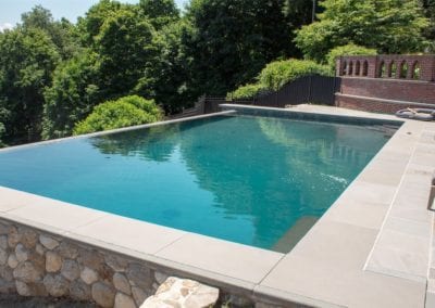 A serene backyard infinity pool with stone detailing on a sunny day, crafted by an expert pool builder.