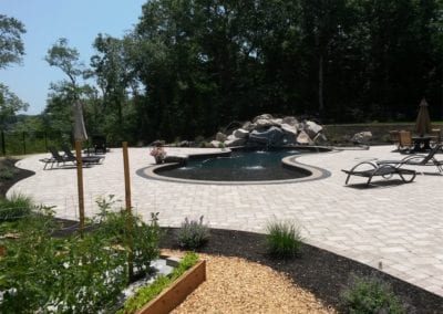 Landscaped backyard with a curved pool designed by a top-rated pool company, and patio area, featuring lounge chairs and a rock waterfall.