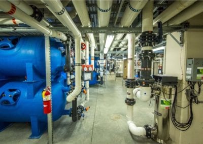 Interior of an industrial mechanical room with pumps, pipes, and valves managed by a premier pool company.