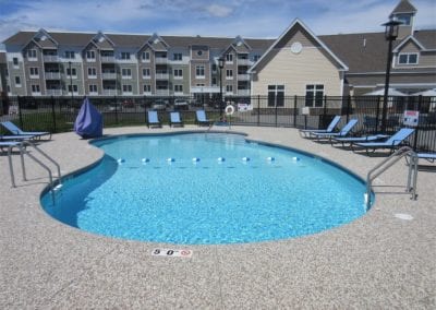 Outdoor swimming pool by a pool company at a residential apartment complex with lounge chairs and clear blue water on a sunny day.