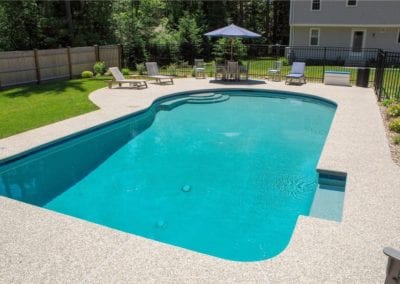 Backyard swimming pool built by a renowned pool company, with patio furniture and a parasol on a sunny day.