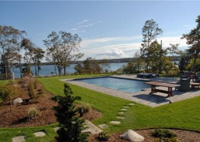 Backyard with a swimming pool, crafted by a prestigious pool builder, overlooking a scenic waterfront view.