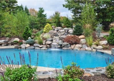 An elegant backyard swimming pool built by a top pool company, with a waterfall and surrounding landscaping.