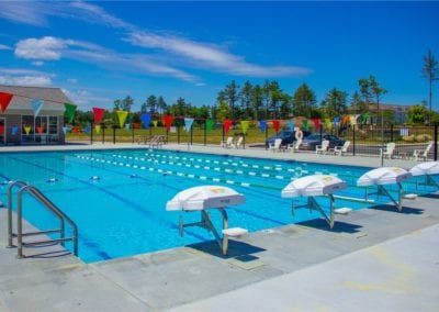 A sunny day at an outdoor community swimming pool built by a top-rated swimming pool company, with lanes marked for swimming, starting blocks, and white umbrellas along the poolside.