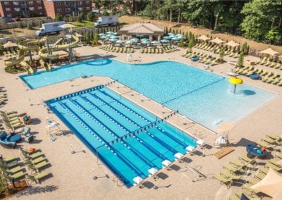 Aerial view of a recreational swimming pool complex, expertly crafted by a top pool builder, with lanes for laps, a leisure pool, water slides, and lounge chairs.