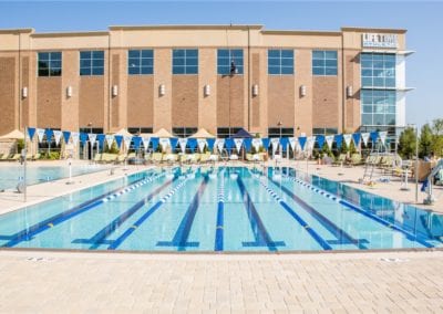 Outdoor swimming pool at a fitness center, constructed by a renowned pool company, with lane markers and poolside loungers.