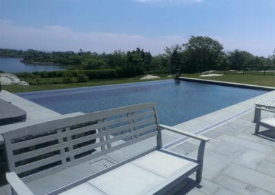 A tranquil swimming pool company-designed outdoor pool overlooking a calm lake with clear skies above.