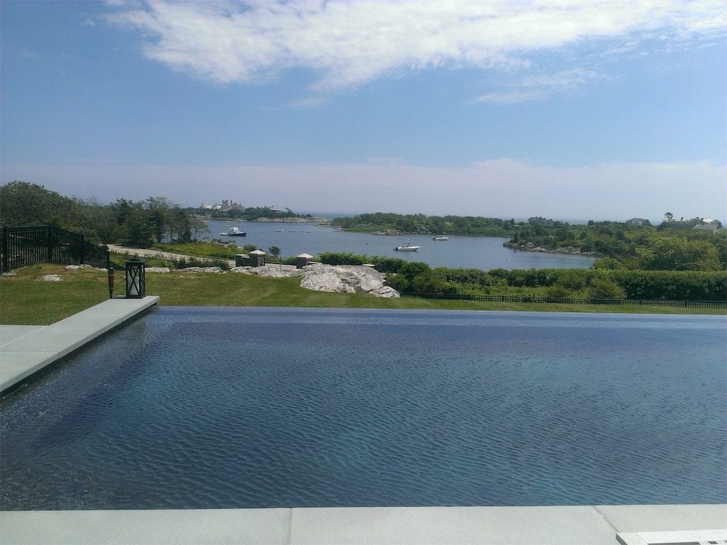 An infinity pool constructed by our premier pool company, overlooking a serene coastal landscape with boats and clear skies.