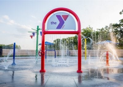 A colorful water playground structure, built by a renowned swimming pool company, with sprinklers featuring the YMCA logo.