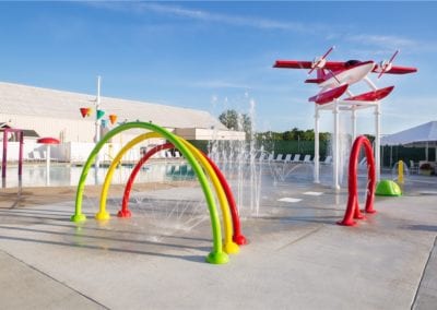Colorful splash pad with water jets and play structures built by a top pool company on a sunny day.