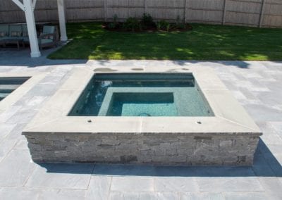 In-ground spa with stone surround in a backyard setting, crafted by a premier pool company.