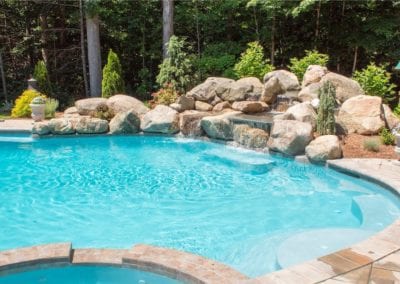 A backyard swimming pool with an integrated rock waterfall feature, designed by a professional pool company.