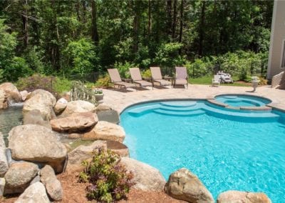 A backyard swimming pool, crafted by a reputable pool company, with a natural stone border and sun loungers on the patio.