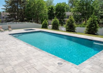 Outdoor residential swimming pool built by a pool company, with surrounding patio and fencing on a sunny day.