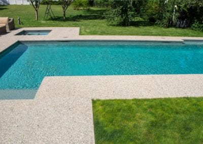 A rectangular swimming pool with clear blue water adjacent to a lawn and patio area, crafted by an expert swimming pool company.