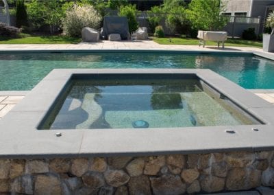 An outdoor swimming pool with an integrated jacuzzi, constructed by a professional pool company, surrounded by patio furniture and landscaping.