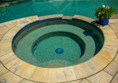 An empty circular spa bath with a stone surround, designed by a leading pool company, adjacent to a larger pool.