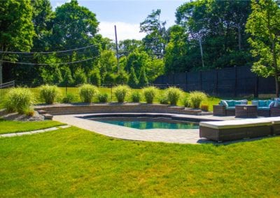 A kidney-shaped backyard swimming pool with surrounding patio and landscaped garden on a sunny day.