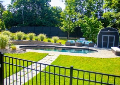 Backyard with a kidney-shaped swimming pool, patio area, and a small shed surrounded by a fence and greenery.