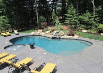 Backyard swimming pool with sun loungers and woodland surroundings, designed by a renowned pool company.