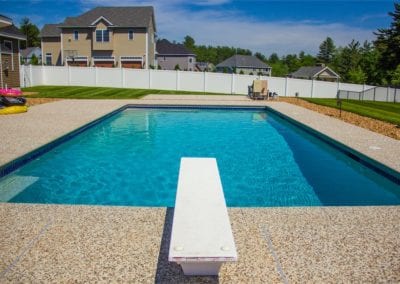 Backyard swimming pool with diving board, constructed by a renowned pool company, and suburban houses in the background.