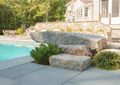 Poolside landscaping by a premier pool builder, featuring natural stone steps leading to a house.