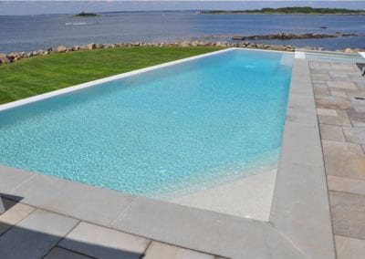 A swimming pool company designed infinity pool overlooking the ocean on a clear day.
