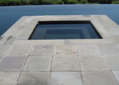An outdoor infinity edge swimming pool company installed with square tiles on the surrounding deck.