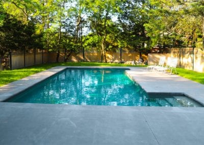 Backyard swimming pool built by a top pool company, with surrounding greenery on a sunny day.