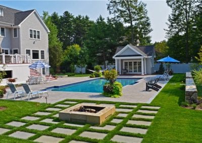 A well-maintained backyard with an in-ground pool by a renowned pool company, pool house, sun loungers, and a fire pit arranged in a landscaped garden.