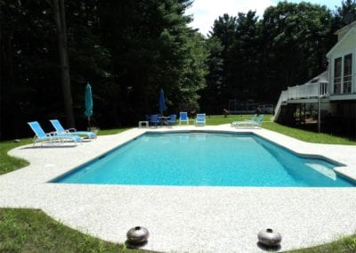 A private backyard with an in-ground swimming pool, crafted by a top-rated pool company, surrounded by lounge chairs and shaded by umbrellas, adjacent to a residential house.