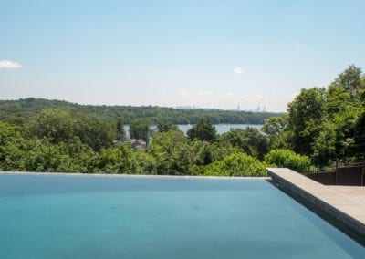Infinity pool designed by a leading pool company, overlooking a forested area with a distant city skyline.