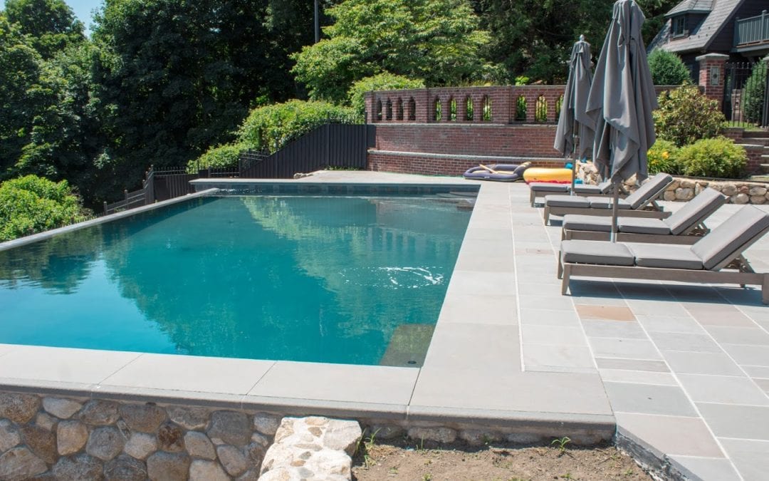 An outdoor swimming pool built by a renowned pool company, featuring lounge chairs and a shaded area in a residential backyard.