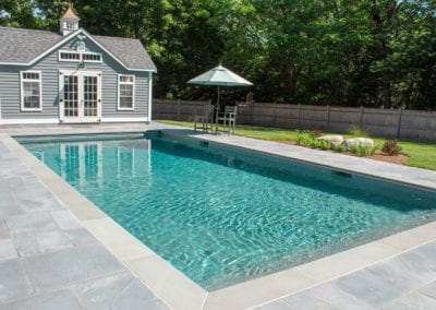 Backyard swimming pool with a pool house and patio area, designed by a renowned pool builder.