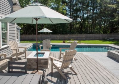 Backyard patio with a dining set and umbrella overlooking a swimming pool built by a top pool company on a sunny day.