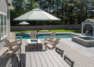 Backyard with a swimming pool built by a swimming pool company, patio furniture, and a sun umbrella on a sunny day.
