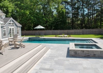 Backyard with a rectangular swimming pool built by a top-rated pool company, hot tub, and wooden deck chairs on a sunny day.